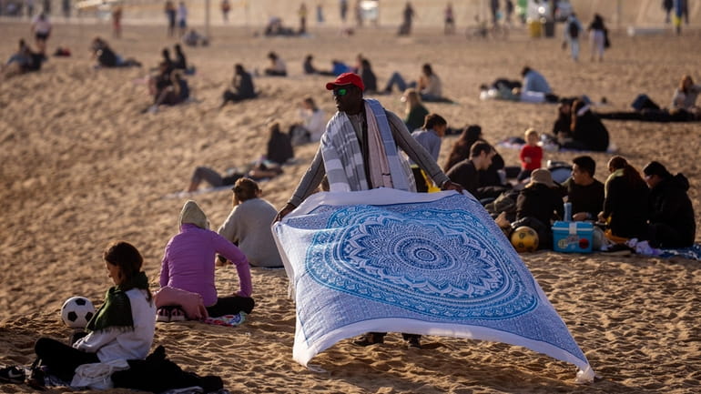 A street vendor displays sheets for sale while people sunbathe...