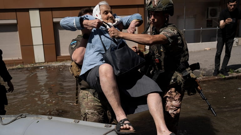 A woman is evacuated from a flooded neighborhood in Kherson,...