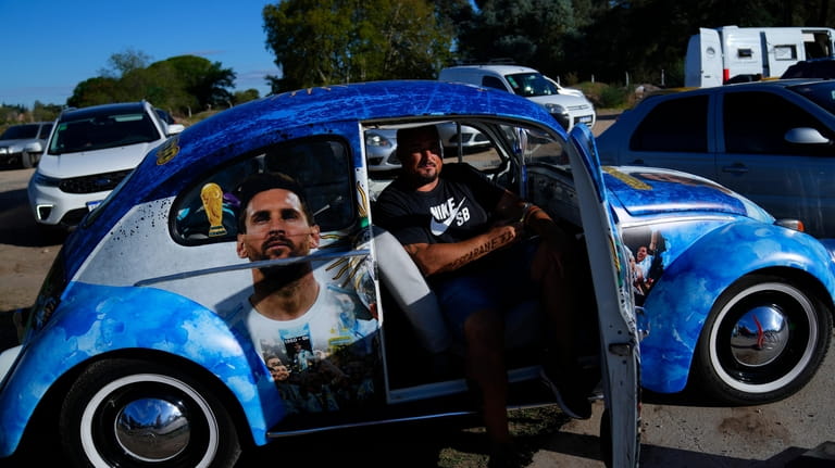 A soccer fan sits in a Volkswagen beetle emblazoned with...