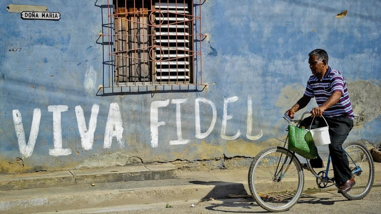 A Cuban rides his bicycle by graffiti hailing former Cuban...