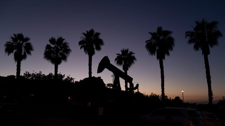 A pump jack sits idle in front of palm trees...