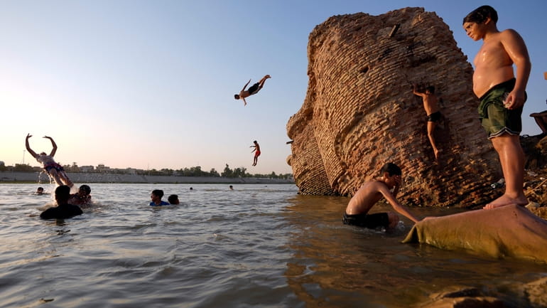 Iraqi men and their sons swim in the Tigris river...