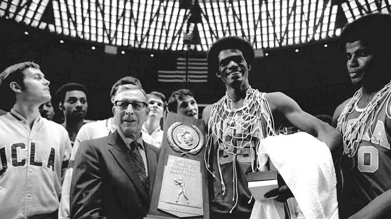 UCLA coach John Wooden holds the NCAA championship trophy which...