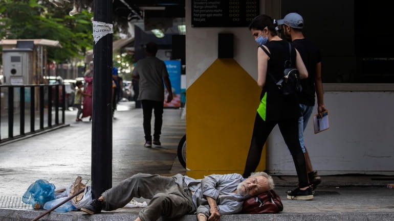 a woman looks at a homeless Lebanese man sleeping on...