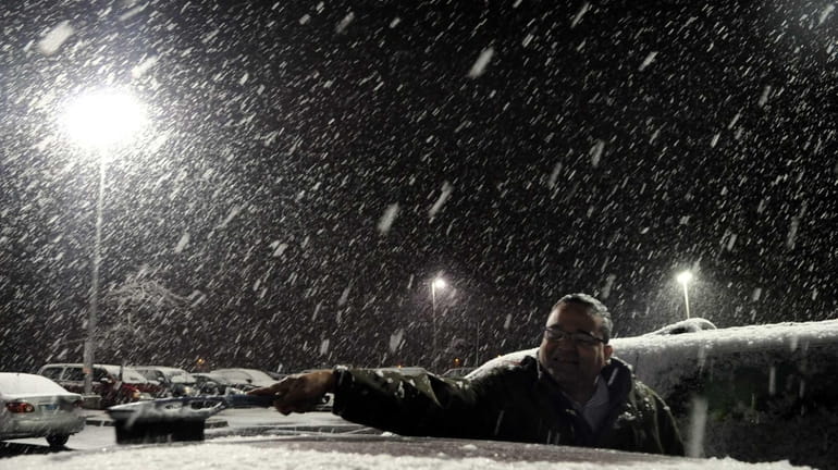 Deepak Tawde, of Plainview, cleans snow off his car after...