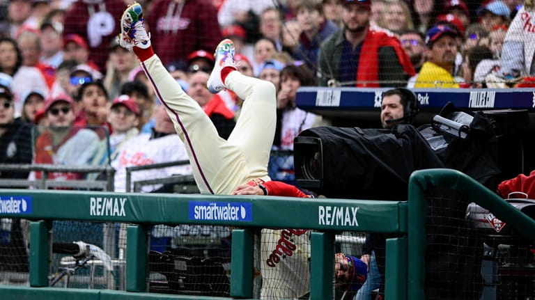 Philadelphia Phillies' Bryce Harper falls into the dugout as he...