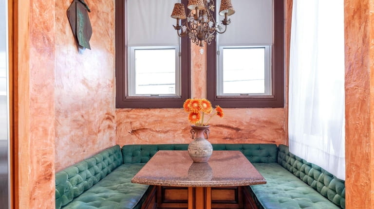 The breakfast nook has a banquette surrounded by stucco walls with a...