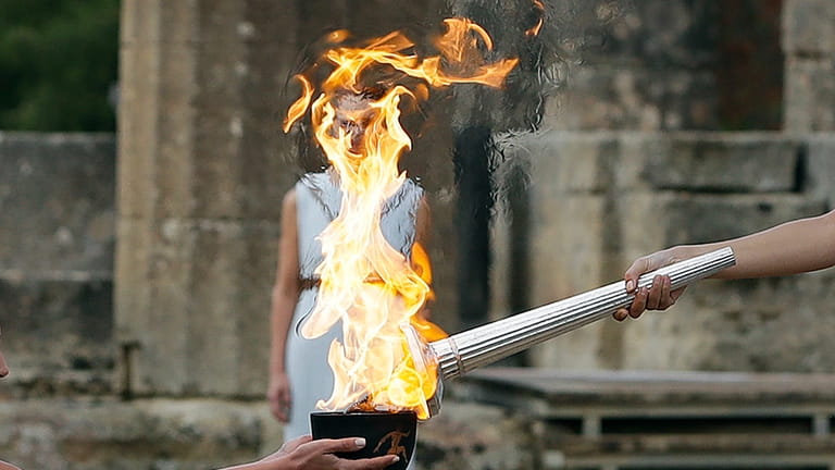 Actress Katerina Lehou, right, as high priestess, lights the torch...