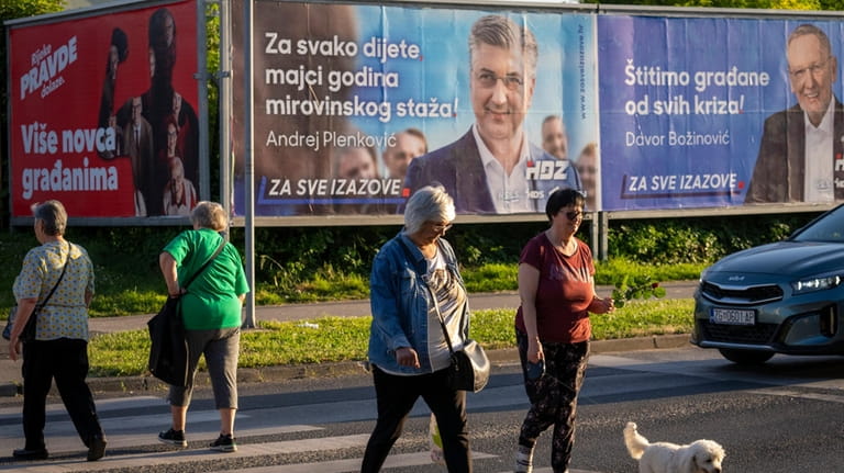 Pedestrians cross a street in front of election posters in...