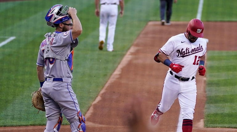 The Nationals' Kyle Schwarber, center, crosses home plate for his...