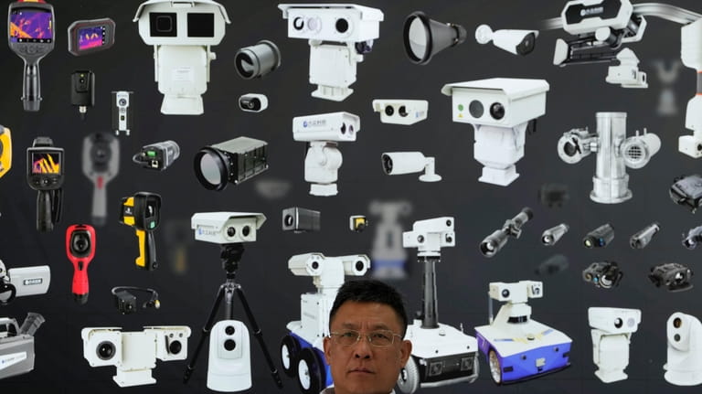 A vendor sits near a board depicting surveillance cameras during...