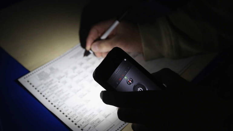 A voter marks his ballot via cell phone light at...