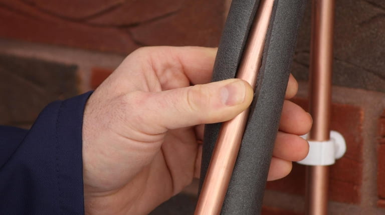 A plumber applies insulation to a copper water pipe.