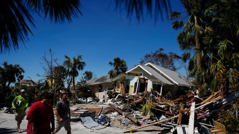Men walk past destroyed homes and debris as they survey...