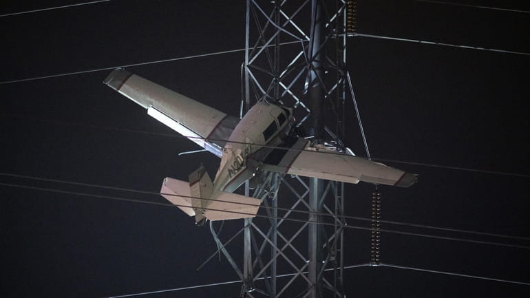 A small plane rests on live power lines after crashing,...