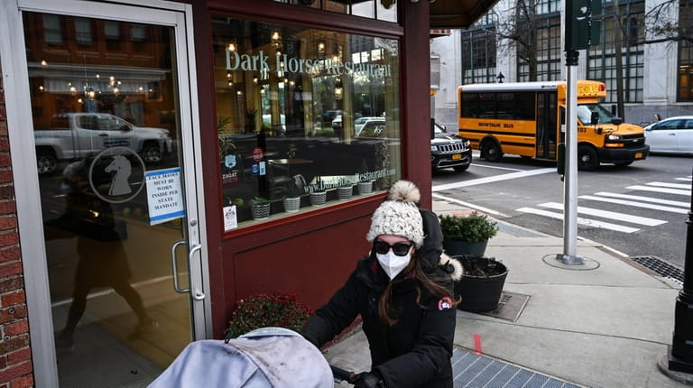 A woman pushing a stroller wears a mask to protect against...
