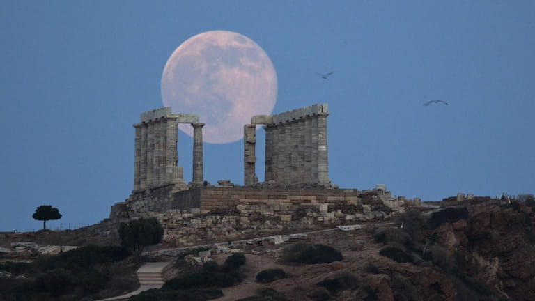 A full moon rises behind the ancient marble Temple of...