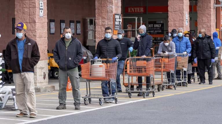 People wearing masks wait in line to enter Home Depot...