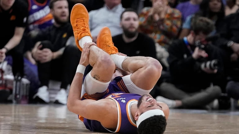 Phoenix Suns guard Devin Booker (1) holds his leg after...