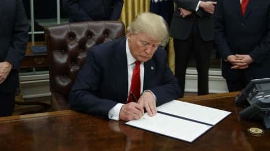 President Donald Trump signs his first executive order, on the...