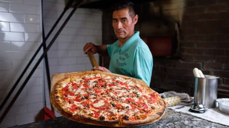 Pizzaiolo Luis Barrera holds a large sausage pizza in front...