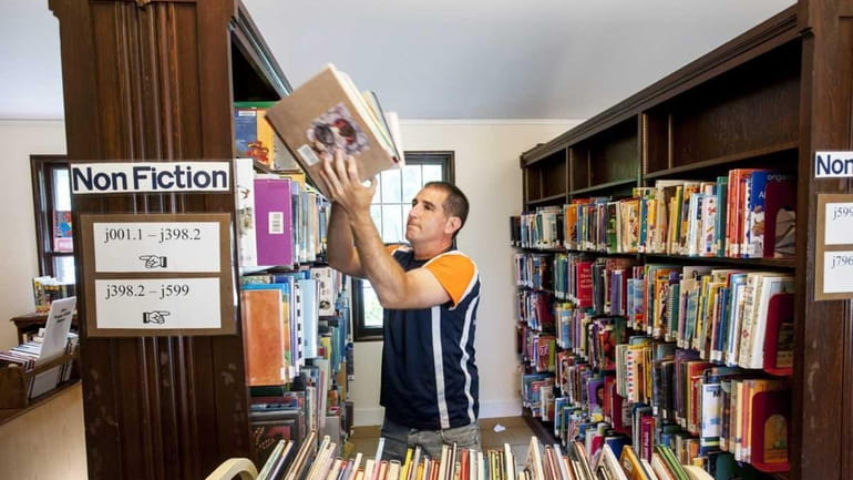East Hampton Library Director Dennis Fabiszak moves books off the...