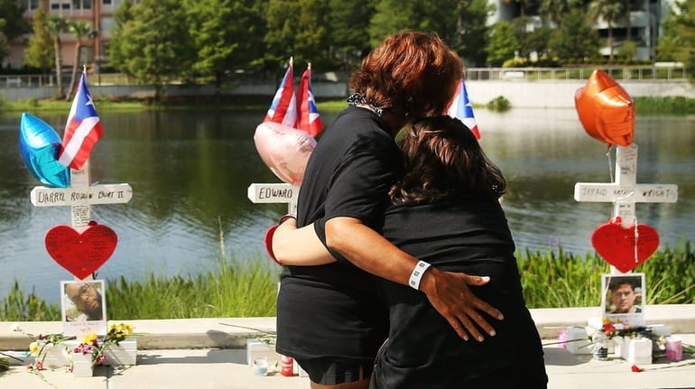 Two women embrace beside a memorial down the road from...
