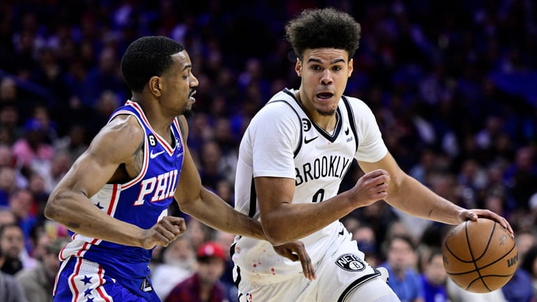 The Nets' Cameron Johnson, right, dribbles the ball past the 76ers'...