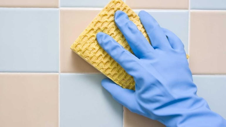 Cleaning the bathroom tiles with a scrubbing pad and gloves.