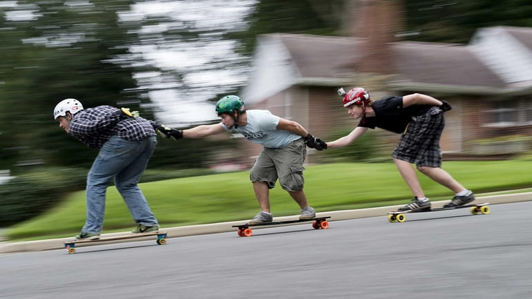 Three skateboarders enjoy the short hill on Fairview Road in...