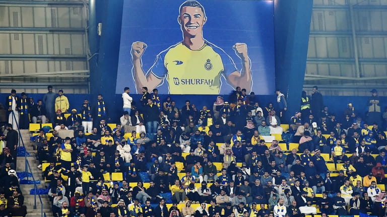 Al Nassr fans sit under a giant billboard of Cristiano...