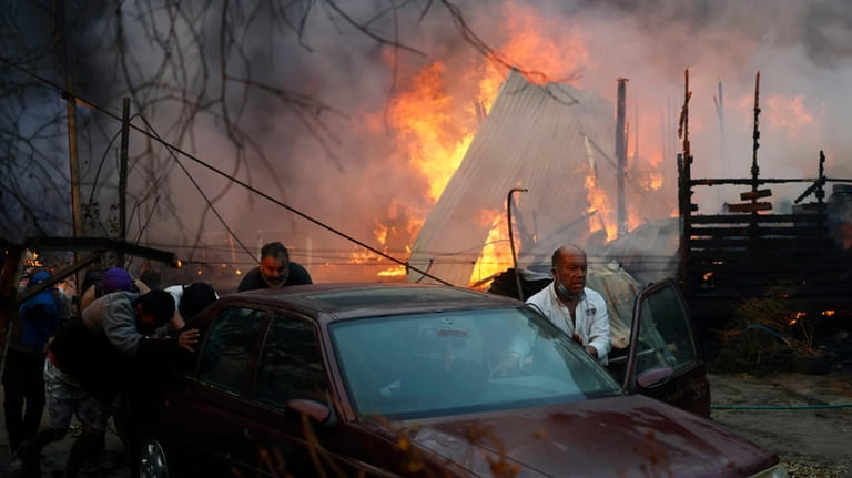 Residents push a car away from a burning forest fire...