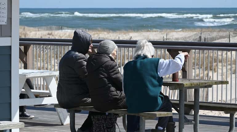 Three women sit at Ponquogue Beach in Hampton Bays on...