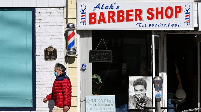 A person walks past Alek's Barber Shop and Santoli TV...