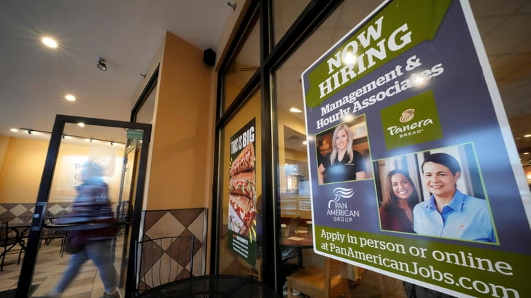 A hiring sign is displayed in the window of a Panera...