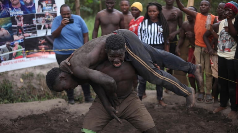 Ugandan youths perform an amateur wrestling tangle in the soft...