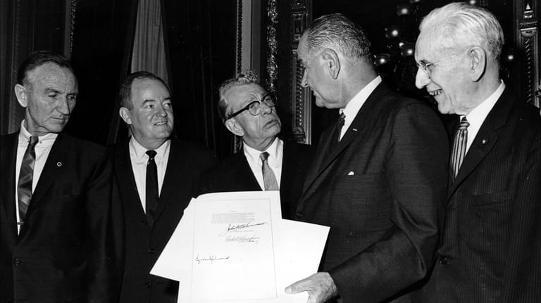 President Lyndon B. Johnson holds the signed document of the...
