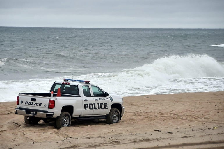 East Hampton Town police drive along the beach at the...
