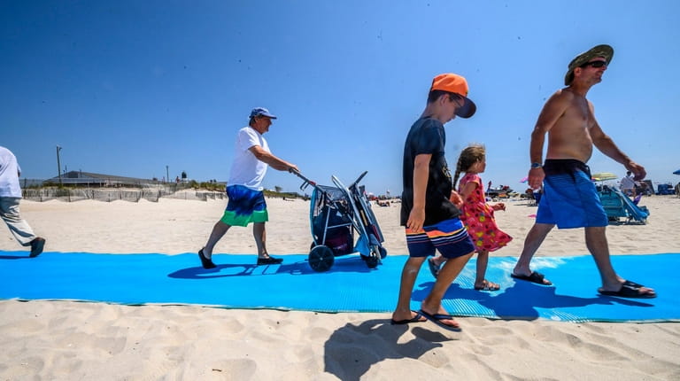 Beachgoers on Friday use new blue mats that make getting onto...