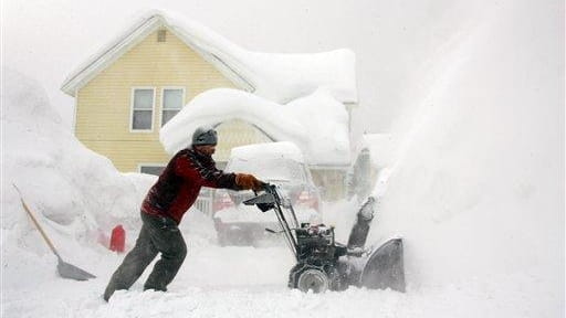 A man uses his snow-blower to remove the snow from...