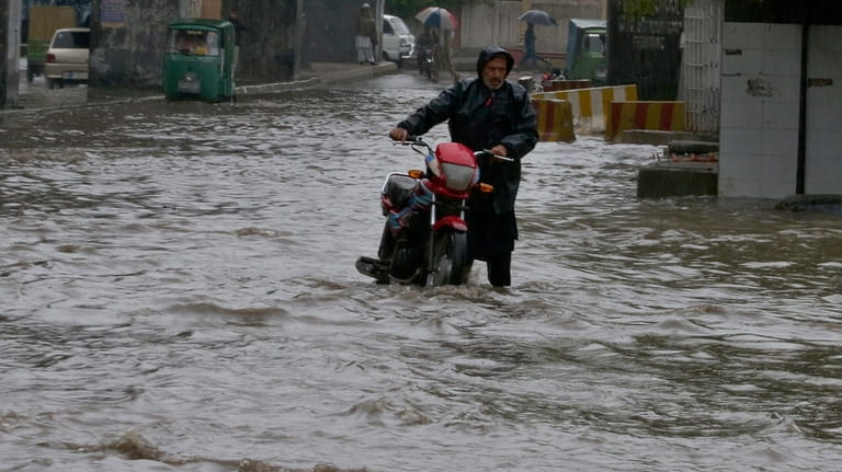 A Pakistani with his bike wades through a flooded road...
