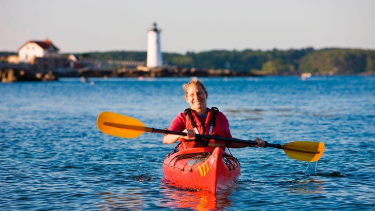 A woman kayaking in New Castle, N.H. Portsmouth Harbor Lighthouse...