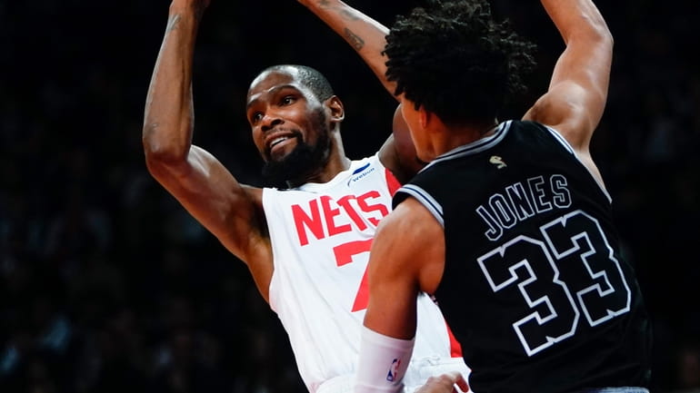 The Nets' Kevin Durant, left, protects the ball from the Spurs'...