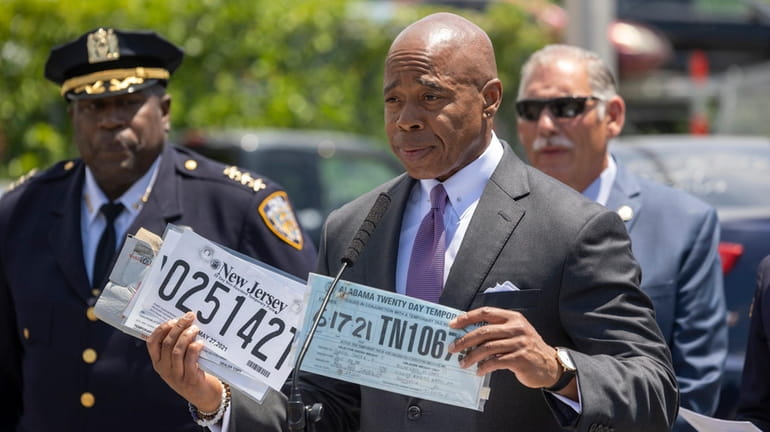 New York City Mayor Eric Adams holds up paper temporary...